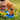 A dog drinks water from a blue collapsible bowl on the grass. A hand is pouring water from a clear bottle into the bowl.